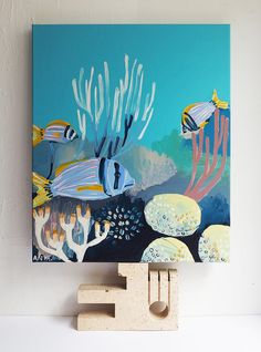 an abstract painting with fish and corals on a blue background is displayed against a white wall