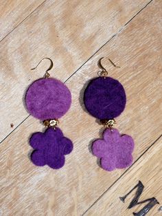 two purple flowers are hanging from earrings on a wooden surface with the word mm written below them