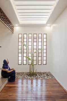 a woman sitting on the floor in front of a bamboo plant and windows with wooden slats