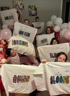 a group of children holding up t - shirts with names on them and balloons in the background