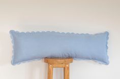 a blue pillow sitting on top of a wooden chair next to a white wall and a stool