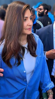 a woman wearing a blue shirt and holding a cell phone in her hand while standing next to other people