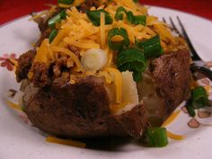 a white plate topped with a baked potato covered in cheese and veggies next to a fork