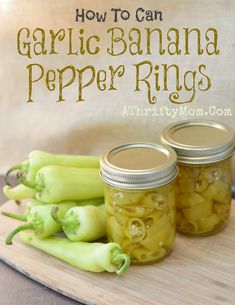 three jars filled with green peppers sitting on top of a wooden cutting board next to other vegetables