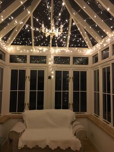 a white couch sitting under a glass roof covered in fairy lights and string lights on the ceiling