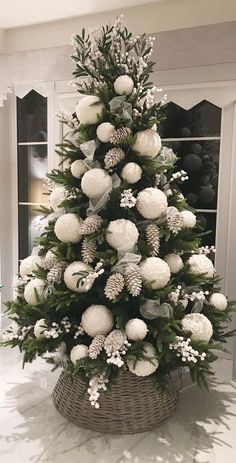 a christmas tree decorated with white balls and greenery in a basket on the floor