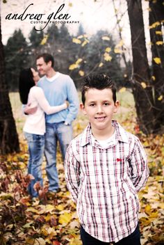 a young boy is standing in the leaves with his parents