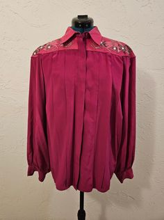 This daring hot pink Western-style button-down collared shirt from Cedars Woman will make you stand out as a retro rodeo queen. Made of silk in a vibrant magenta color, the shirt features a leather collar and yoke with snakeskin appliques adorned with beads, rhinestone gems, and silver embroidered abstract designs. The body of the blouse is made of silk and is pleated at the front under the yoke. The cuffs and front close with buttons, with a placket hiding the buttons down the front. The shirt Rhinestone Blouse, Rhinestone Embroidery, Rodeo Queen, Magenta Color, Fashion Moodboard, Mood Board Fashion, Abstract Designs, Leather Collar, Pink Rhinestones