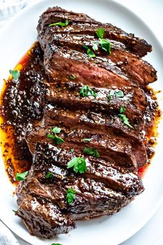 grilled steak on a white plate with sauce and parsley sprinkled on top