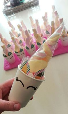 a person holding up a cup with candy in the shape of unicorns on it