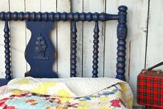 a bed with a quilt on top of it next to a red suitcase and wooden wall