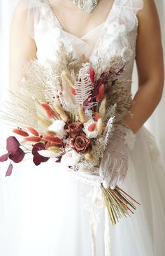 a woman in a white dress holding a bouquet with feathers and flowers on it's side