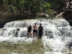 three people standing in front of a waterfall with water running over it and trees behind them