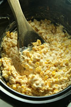 a wooden spoon stirring corn into a crock pot