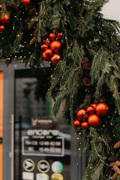 a christmas wreath with red balls and pine cones hanging from it's front door