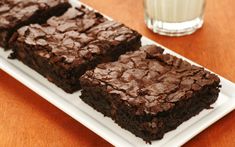 three brownies on a white plate next to a glass of milk and a drink