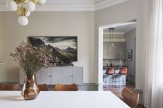 a vase filled with flowers sitting on top of a white table next to a painting