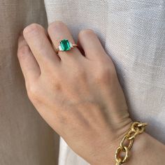 a woman's hand wearing a gold bracelet with an emerald stone on the clasp