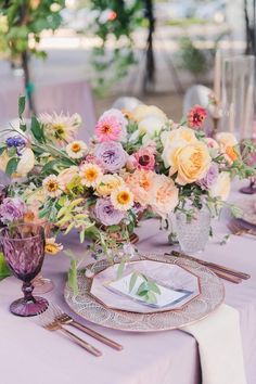 the table is set with purple and yellow flowers in vases, silverware, and napkins