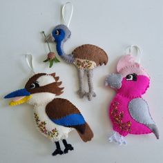 three felt birds hanging from strings on a white surface with one bird holding a flower in it's beak