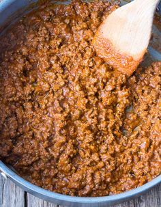 a wooden spoon in a pot filled with chili and meat sauce on top of a table