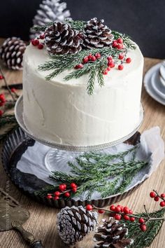 a white frosted cake with pine cones and red berries on top, sitting on a wooden table