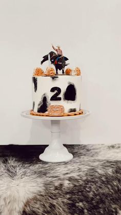 a white cake with black and orange frosting on a table next to a cow skin rug