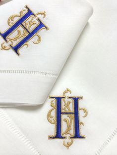 two embroidered monogrammed napkins with the letter h on them, sitting next to each other