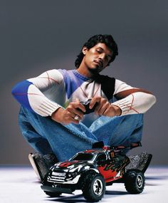 a young man sitting on the ground next to a toy truck and remote control car