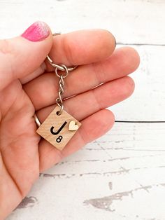 a person holding a wooden keychain with the letter j on it's side