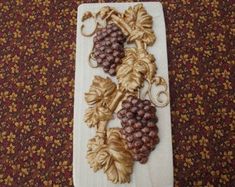 some grapes and leaves are on a white board with gold trimmings, sitting on a carpeted surface