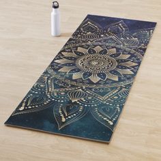 a yoga mat with an intricate blue and gold design on it next to a water bottle