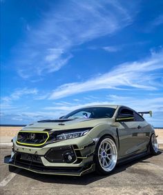 the front end of a gray sports car parked in a parking lot with blue sky and clouds