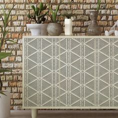 a white cabinet with plants and vases on it in front of a brick wall