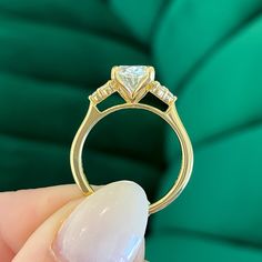 a hand holding a diamond ring in front of a green cushioned background, with the center stone being held up to the camera