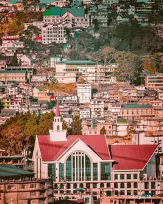 a large building sitting on top of a lush green hillside next to a city filled with tall buildings