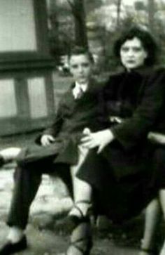 black and white photograph of two people sitting on a bench in front of a house