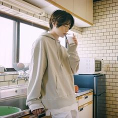 a person standing in a kitchen drinking from a cup and looking at something on the counter