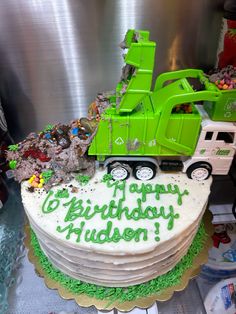 a birthday cake with a dump truck on top and green frosting that says happy birthday hudson