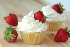 three cupcakes with white frosting and strawberries on a wooden table next to each other