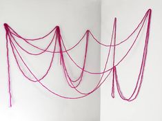 two pictures with red string hanging on the wall and one has pink thread attached to it