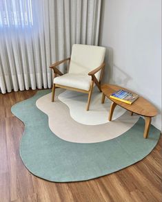 a living room with a chair, table and rug on the floor in front of a window