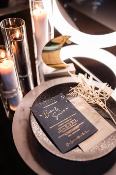 a black and gold wedding card on a silver plate with candles in the back ground