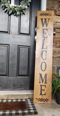 a wooden welcome sign sitting in front of a door with a wreath on the side