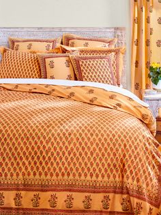 a bed with yellow and red comforters in a bedroom next to a vase filled with flowers