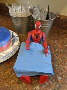 a toy spider man sitting on top of a blue cloth next to two buckets