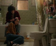 two women sitting on the floor in a bathroom next to a toilet and bathtub