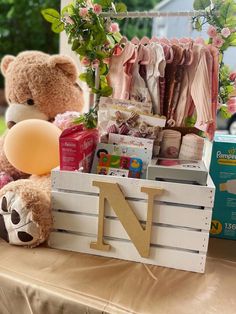 a teddy bear sitting on top of a wooden crate filled with baby clothes and other items