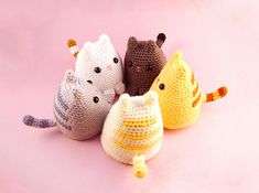 four crocheted cats sitting next to each other on a pink surface with one cat looking at the camera