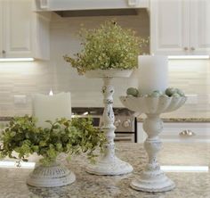 two white vases filled with plants on top of a kitchen counter next to candles